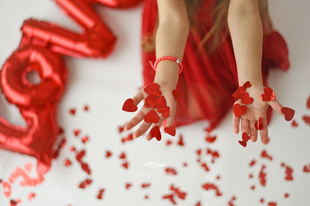 A row of small hands covered in bright red paint making messy handprints on a white surface.