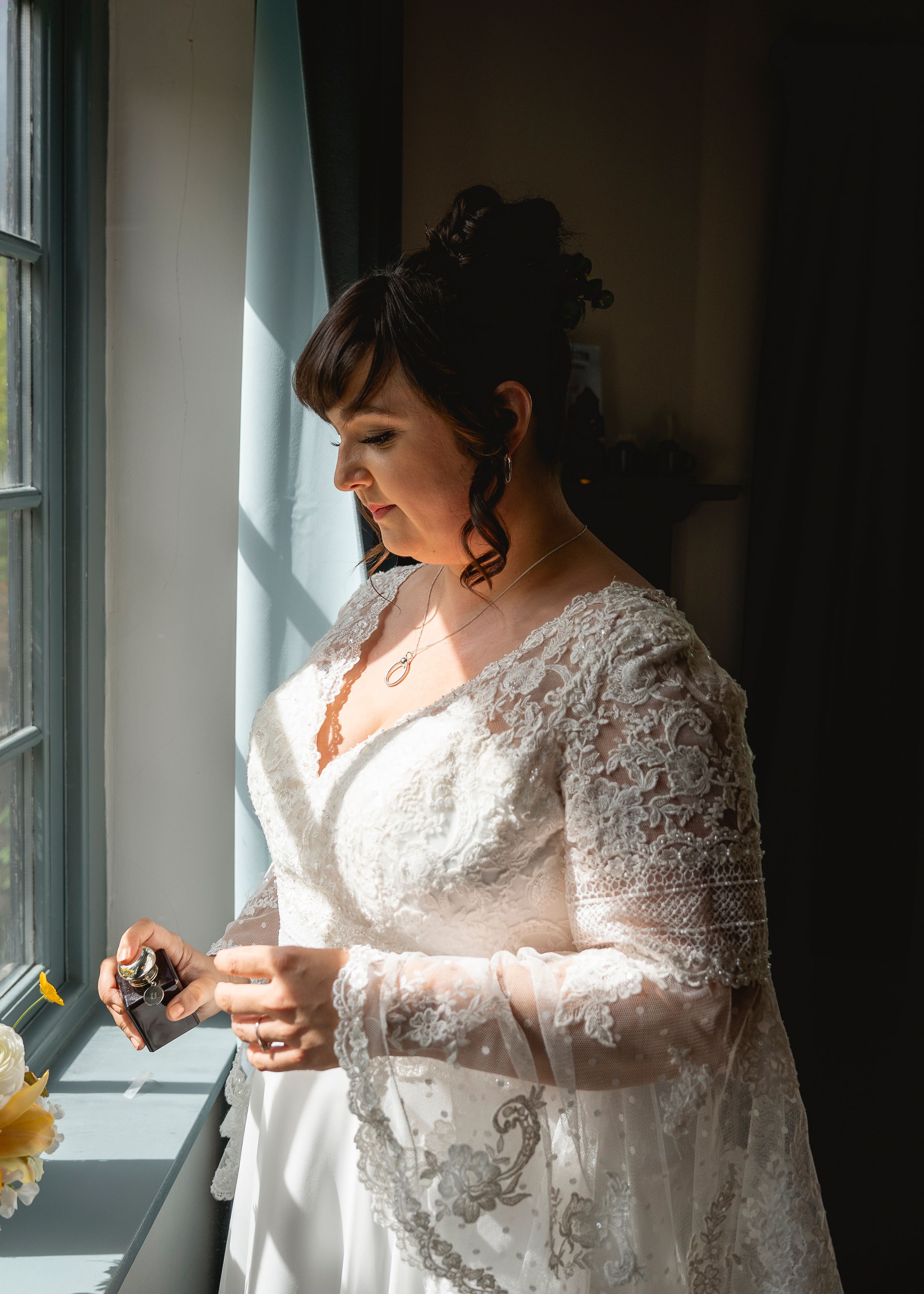 A lace wedding dress silhouetted against window light in a getting-ready sequence.