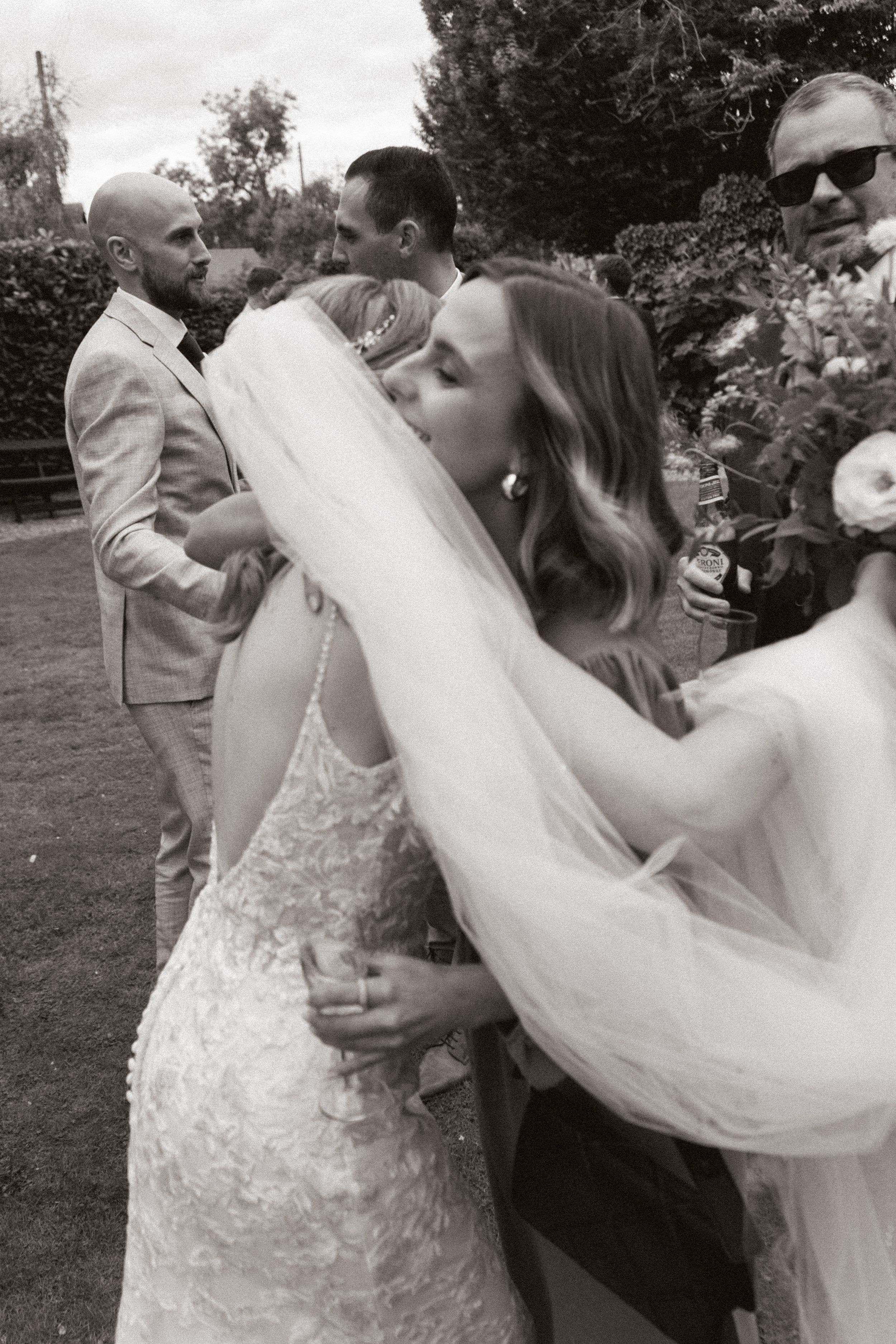 Black and white candid wedding celebration photo in garden setting.