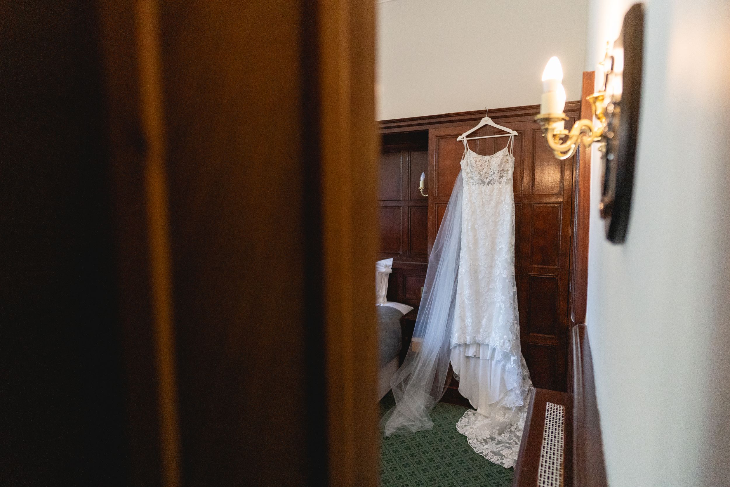 White lace wedding dress hanging elegantly in room with candlelit sconce.