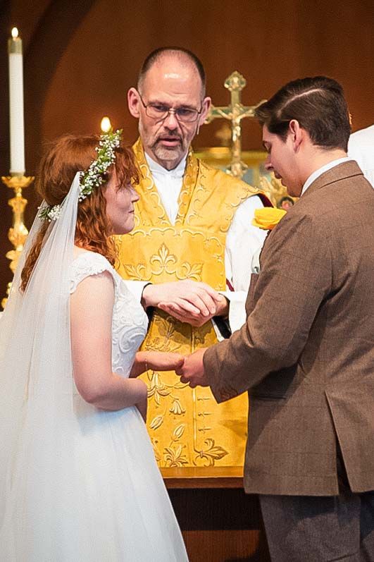 Bride and groom exchange rings during church wedding ceremony with officiant in gold vestments.