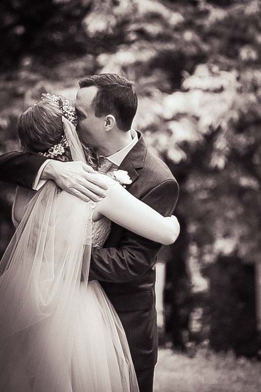 Black and white photo of a bride and groom sharing a romantic kiss outdoors on their wedding day.