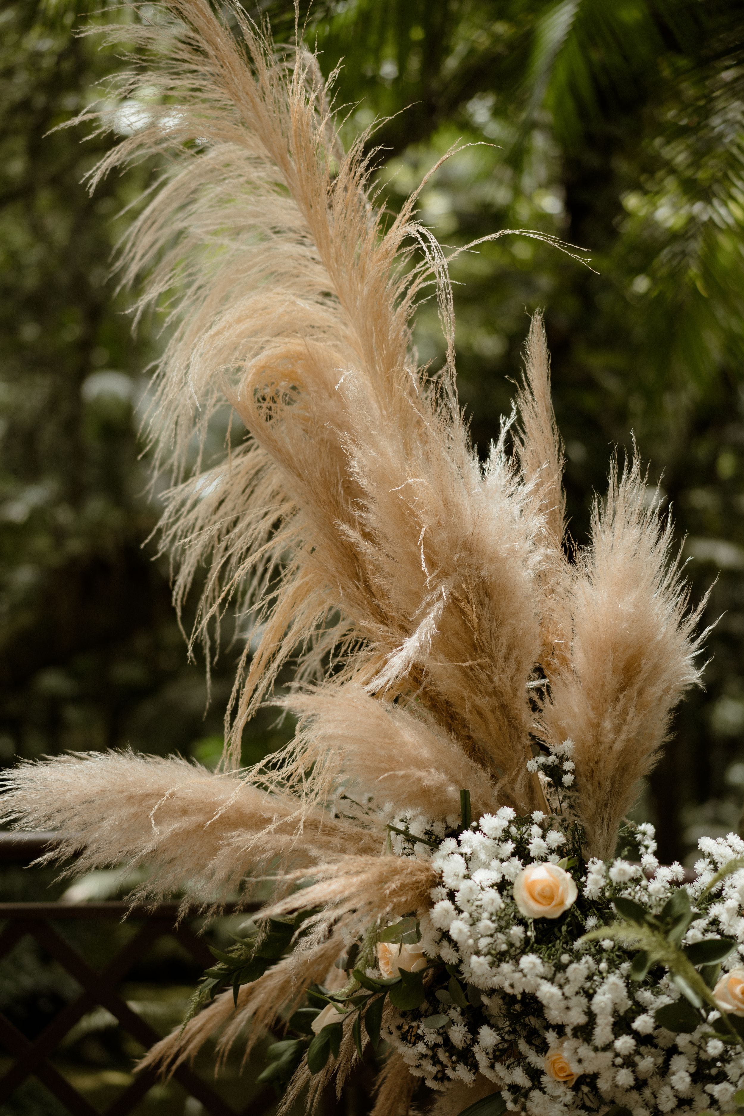 Pampas grass and dried flower arrangement in neutral tones against green background.