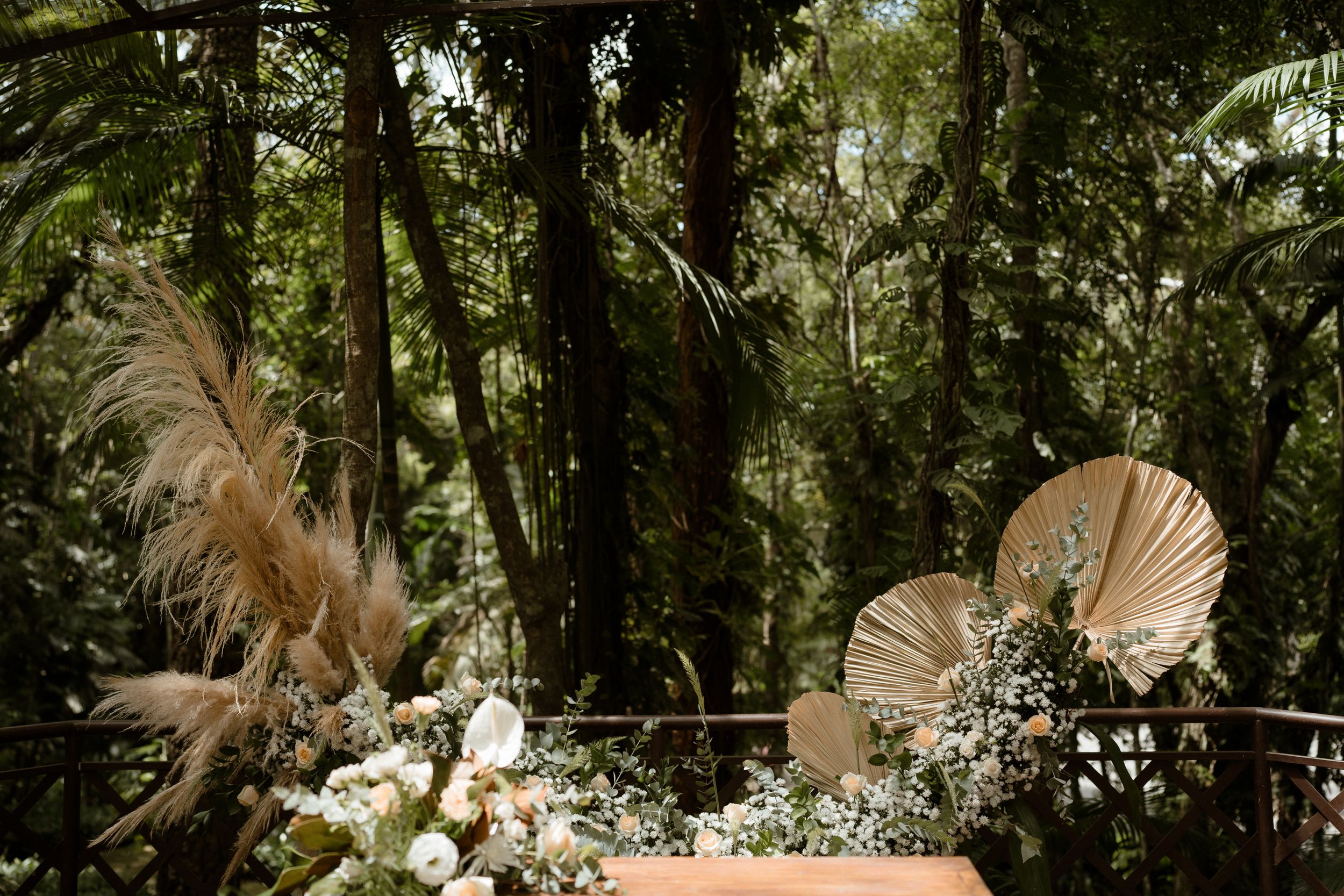 Pampas grass and white floral wedding ceremony decorations adorn a natural outdoor setting.