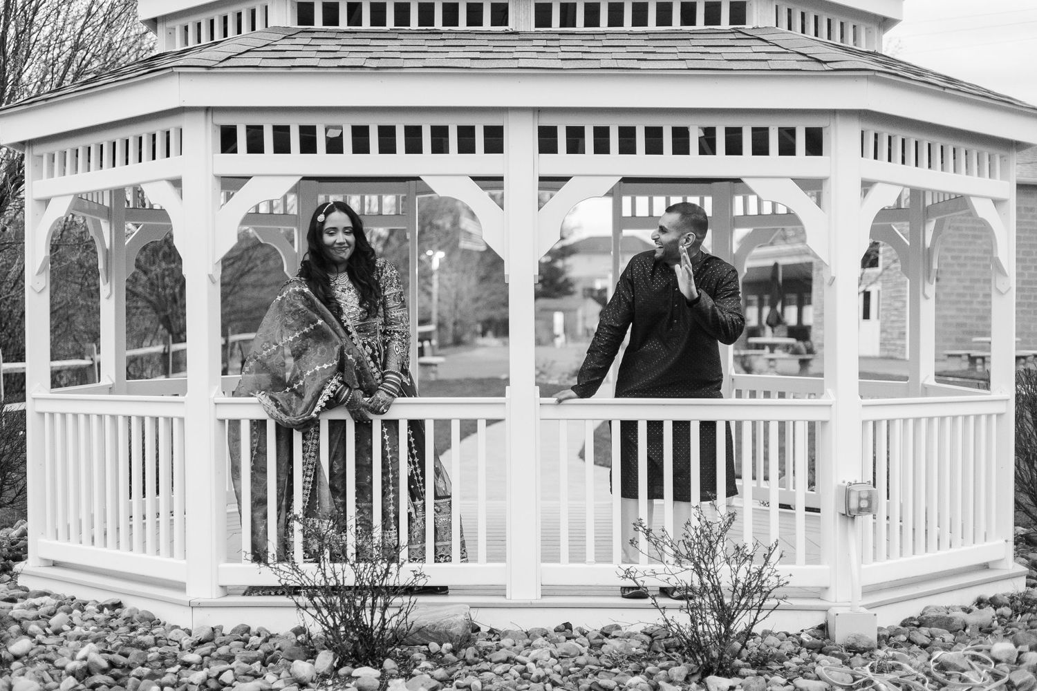 Black and white panoramic view of couple at white gazebo with architectural details.
