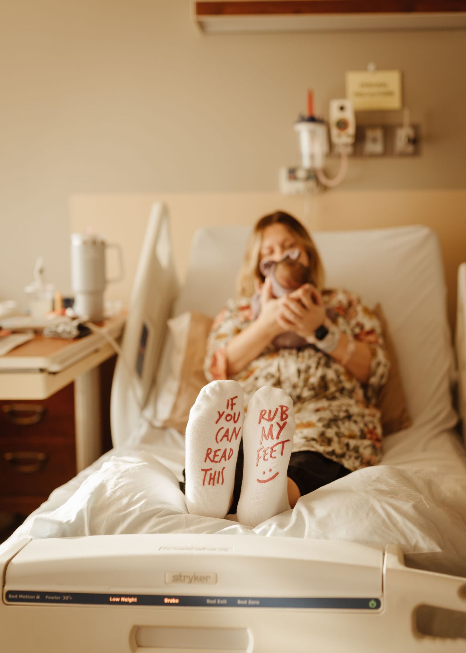 Hospital patient resting in bed wearing floral dress with message written on socks.