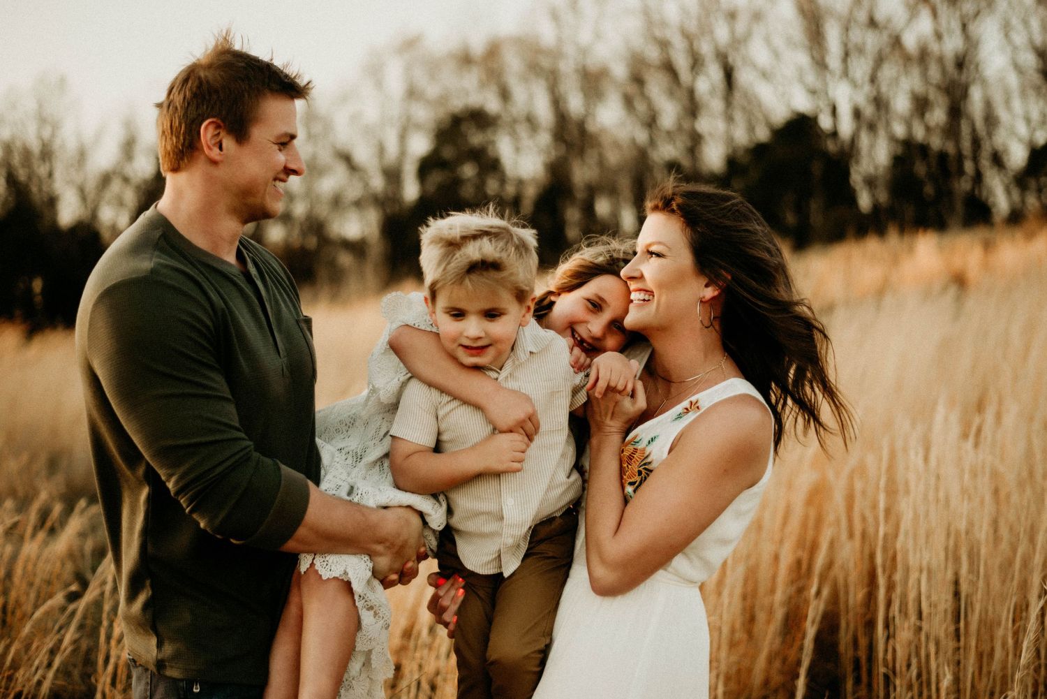 Family laughing together in golden prairie grass at sunset.