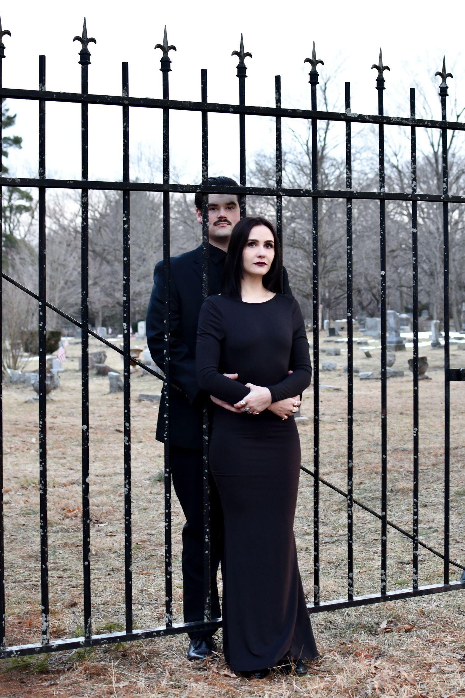Goth couple hugging through cemetery gate.