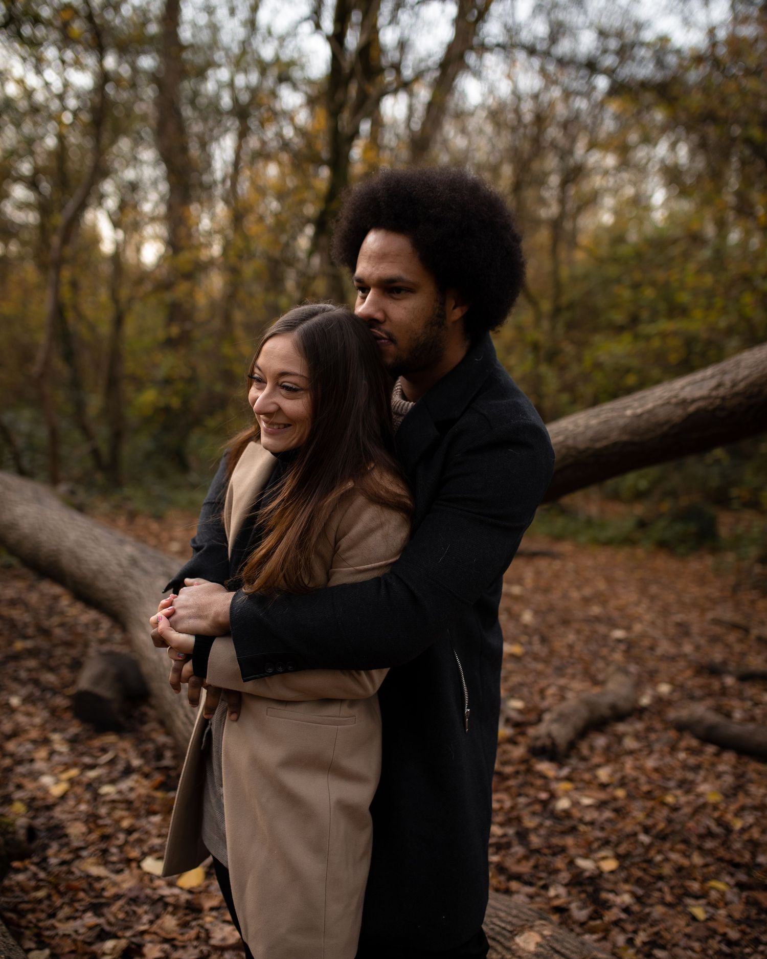 Couple sharing tender embrace among fallen autumn leaves in wooded setting.