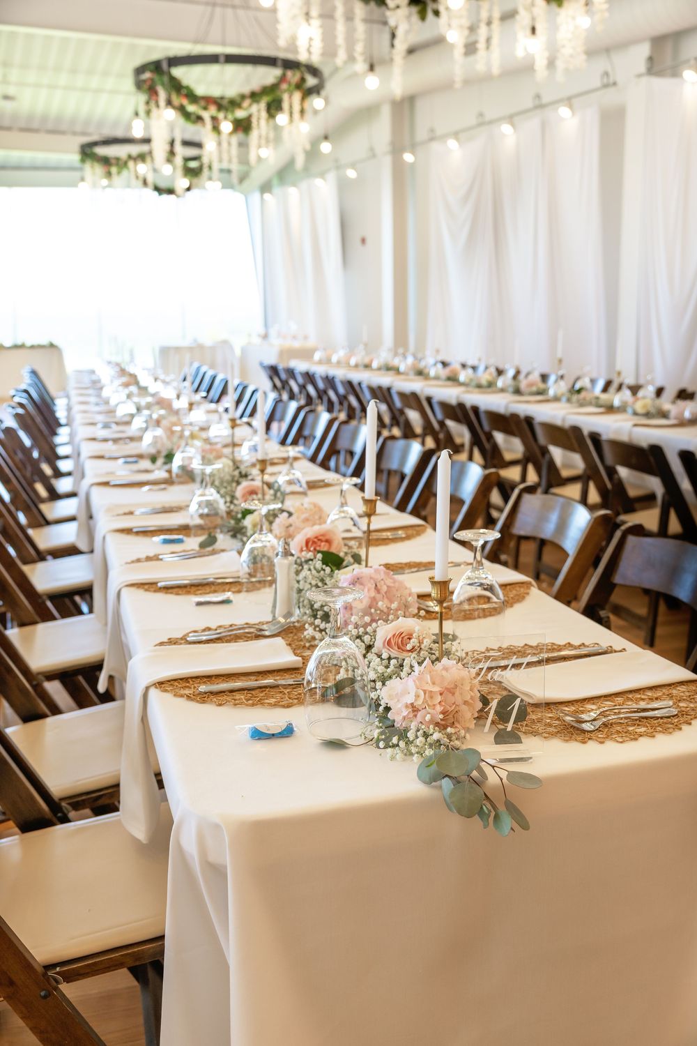Elegant wedding reception tables with white linens, gold runners, pink floral centerpieces, and candles.