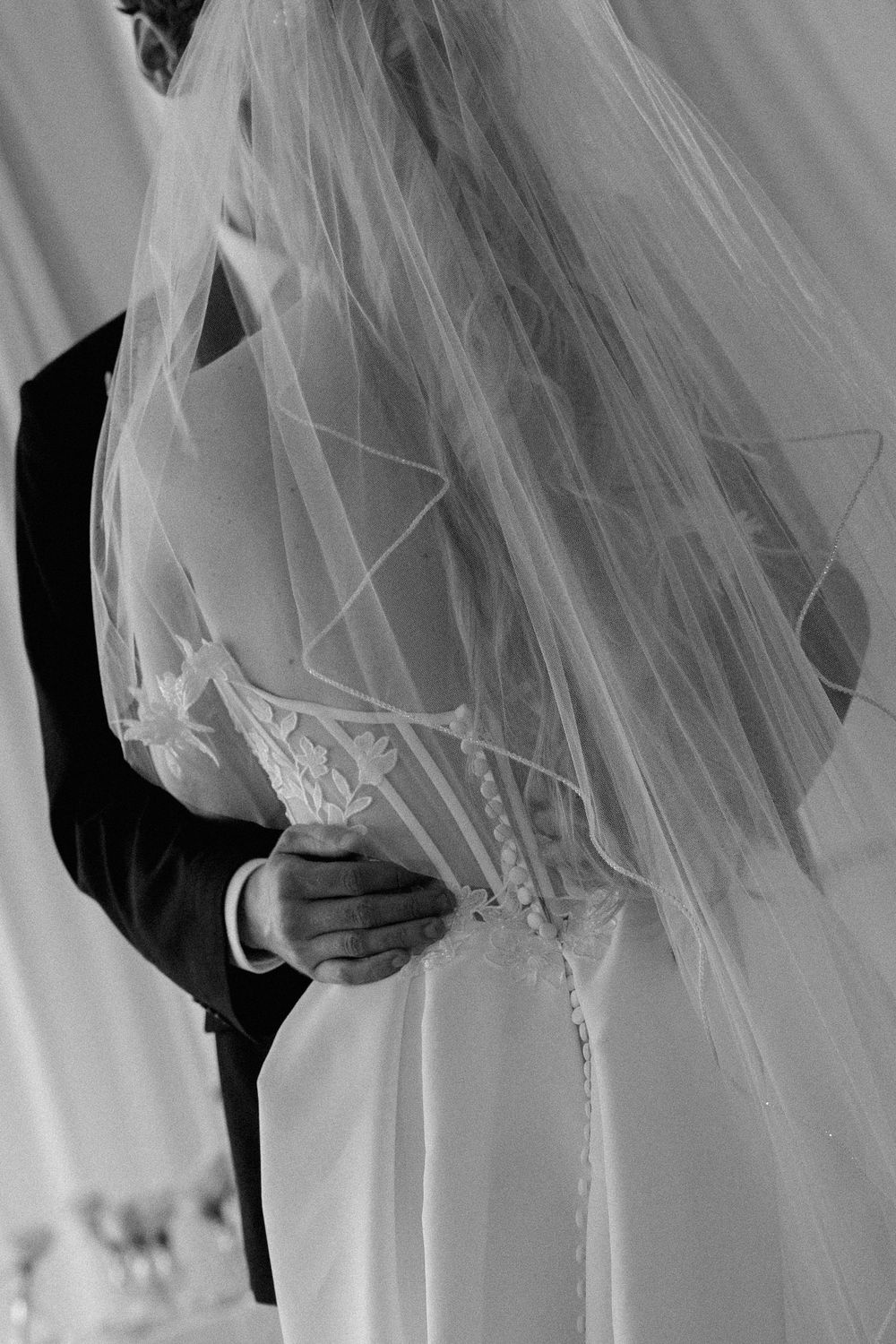 Black and white close-up of groom holding bride in lace wedding dress during their wedding ceremony.