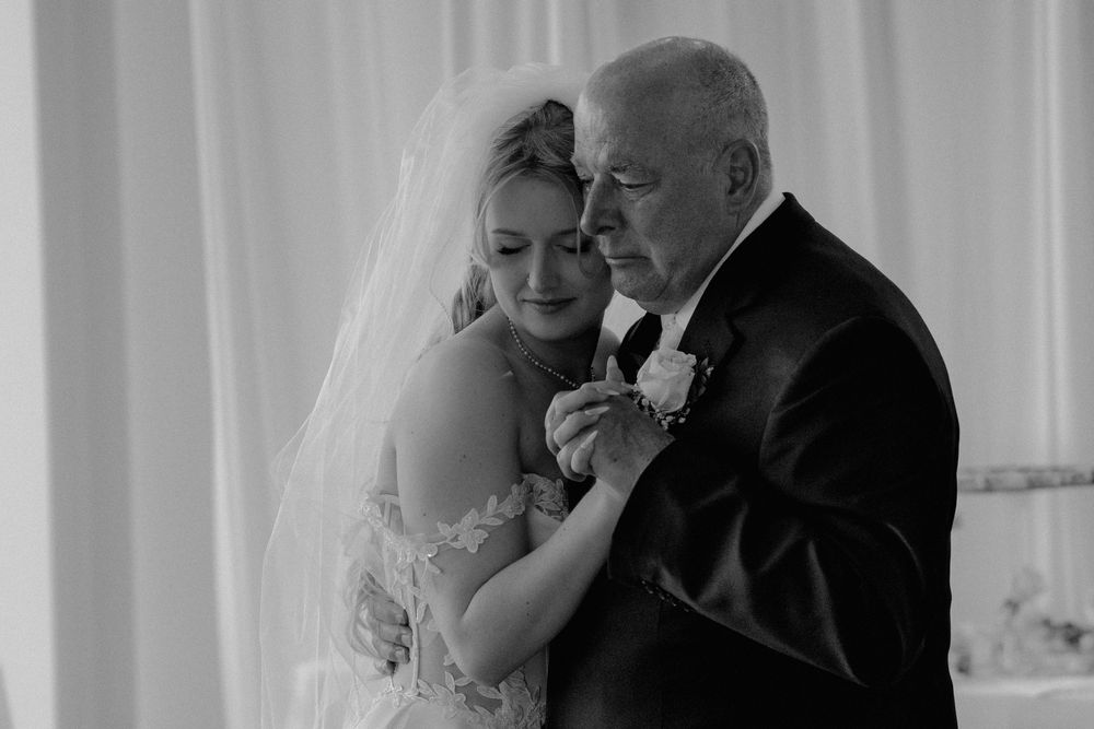 Black and white photo of bride sharing an emotional father-daughter dance at wedding reception.