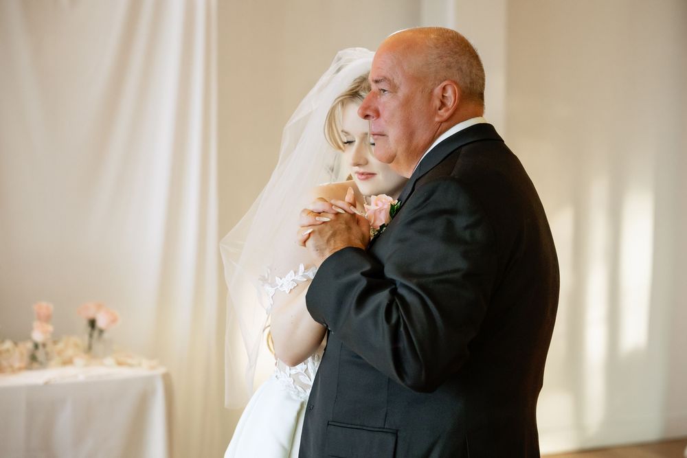 Bride and older gentleman share an emotional father-daughter dance at elegant wedding reception.