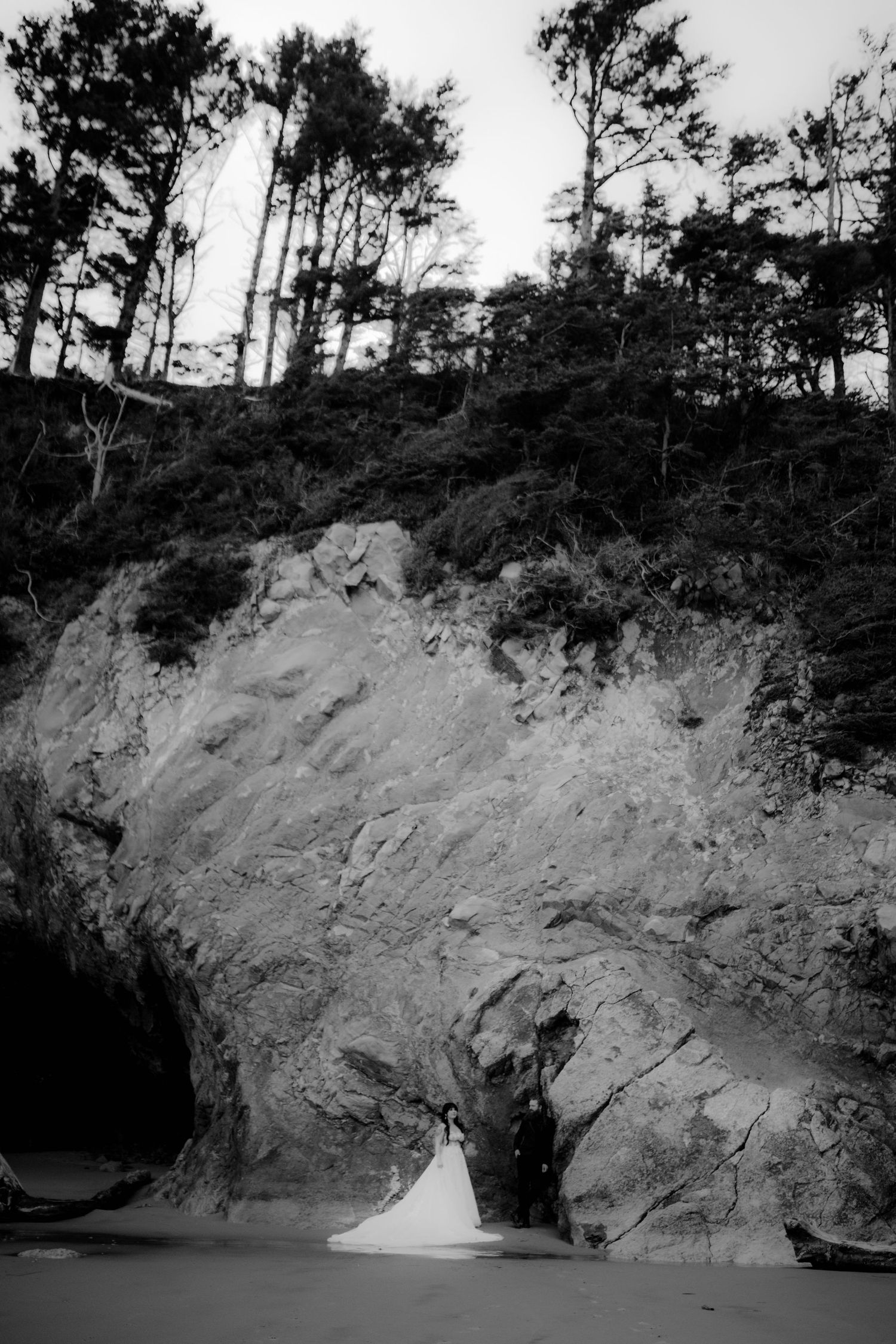 Black and white landscape of a rocky cliff face with trees silhouetted against the sky.