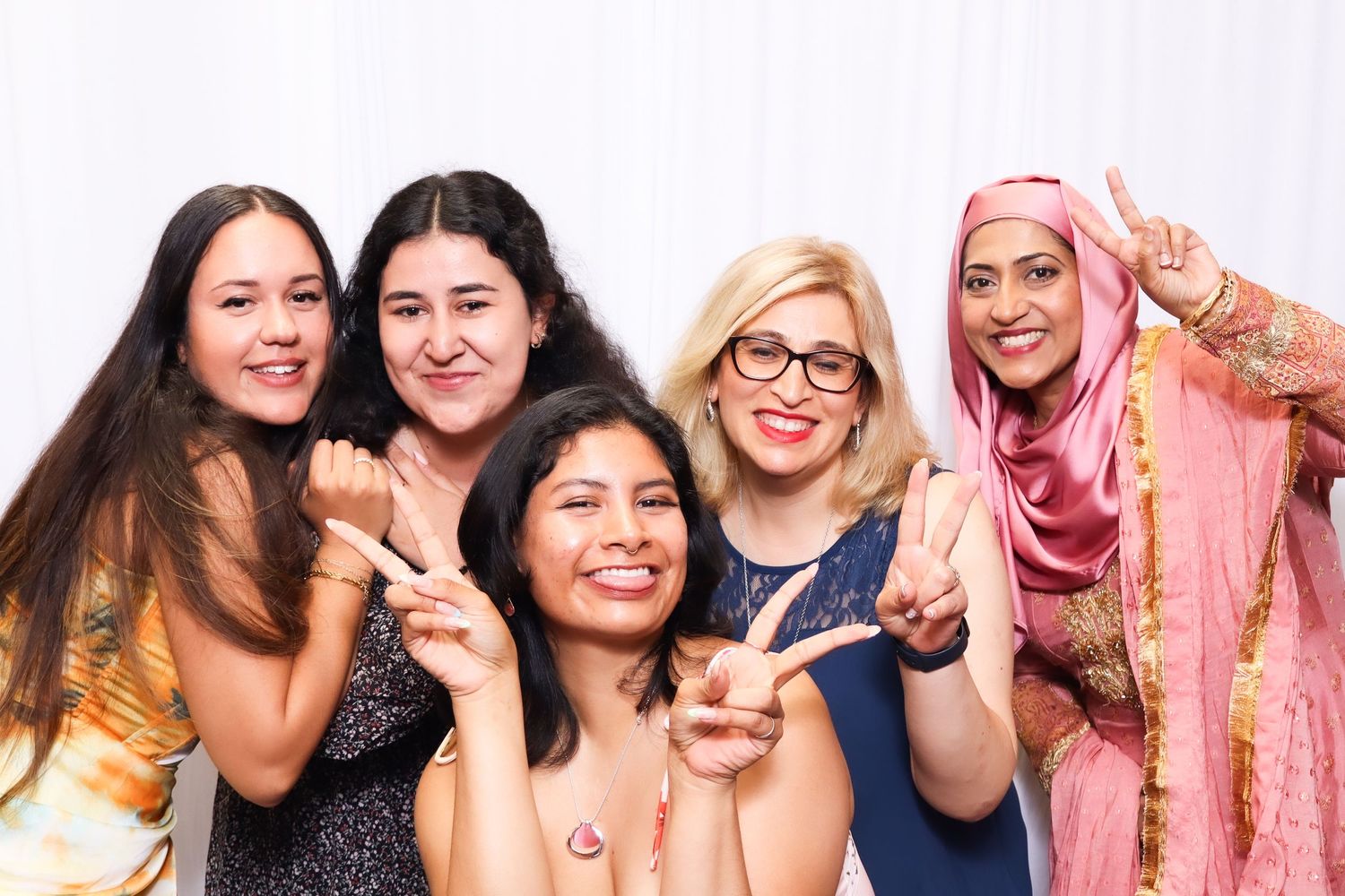 Diverse group of friends in formal attire pose together making peace signs against white backdrop.
