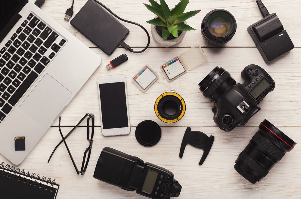 Flat lay of photography gear including DSLR camera, lenses, laptop, and accessories.