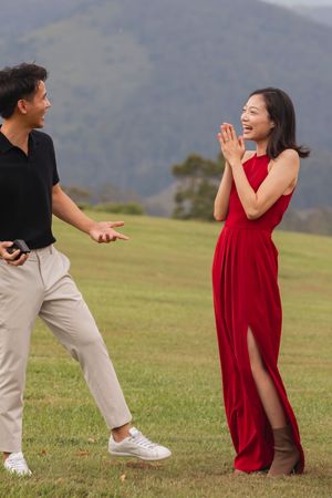 Couple celebrates engagement in red dress and khakis on mountain meadow.