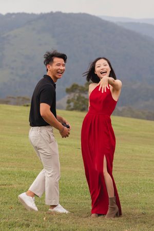 A couple in red and black outfits dances playfully in a hilltop meadow.