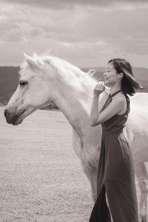A white horse and person share a tender moment in a black and white photograph on a grassy field.