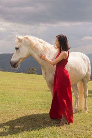 Beautiful white horse stands majestically in mountain pasture with woman in red.