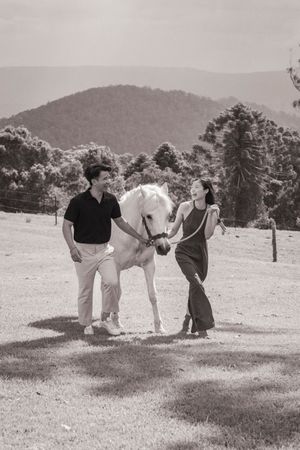 Black and white photo of couple with white horse in countryside setting.