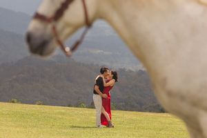 Couple shares romantic moment in mountain field with white horse.