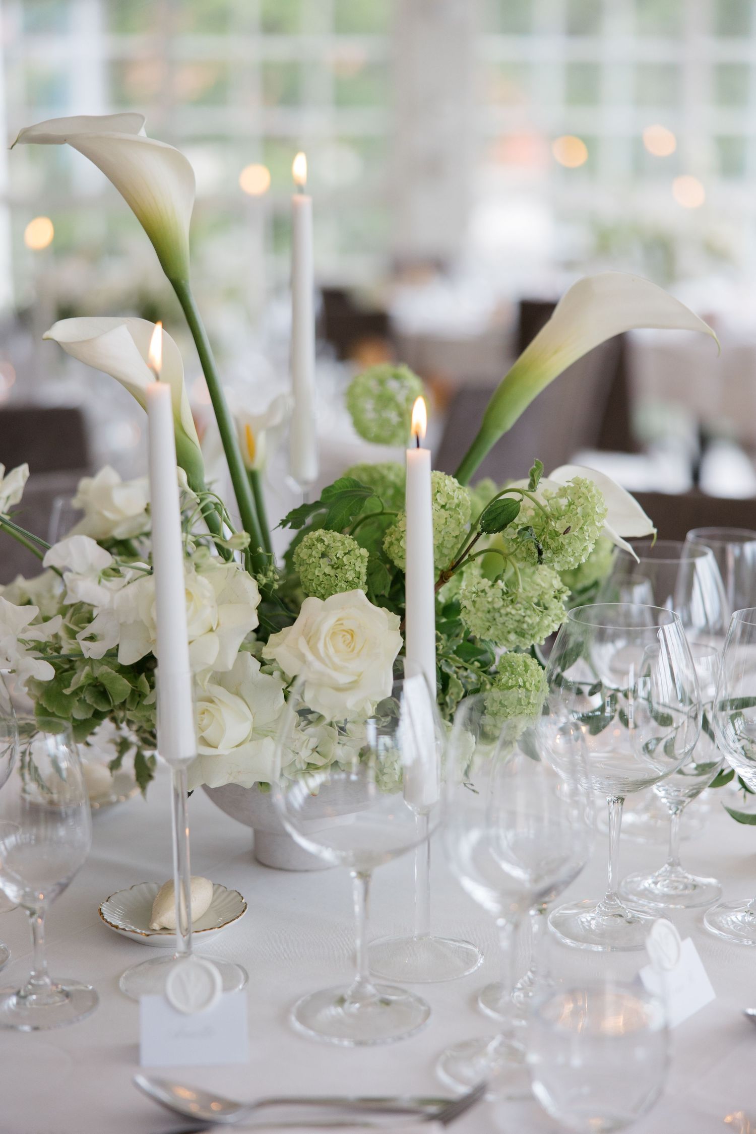 Elegant table setting with tall taper candles, eucalyptus garland, and dark ceramic plates on white linens.