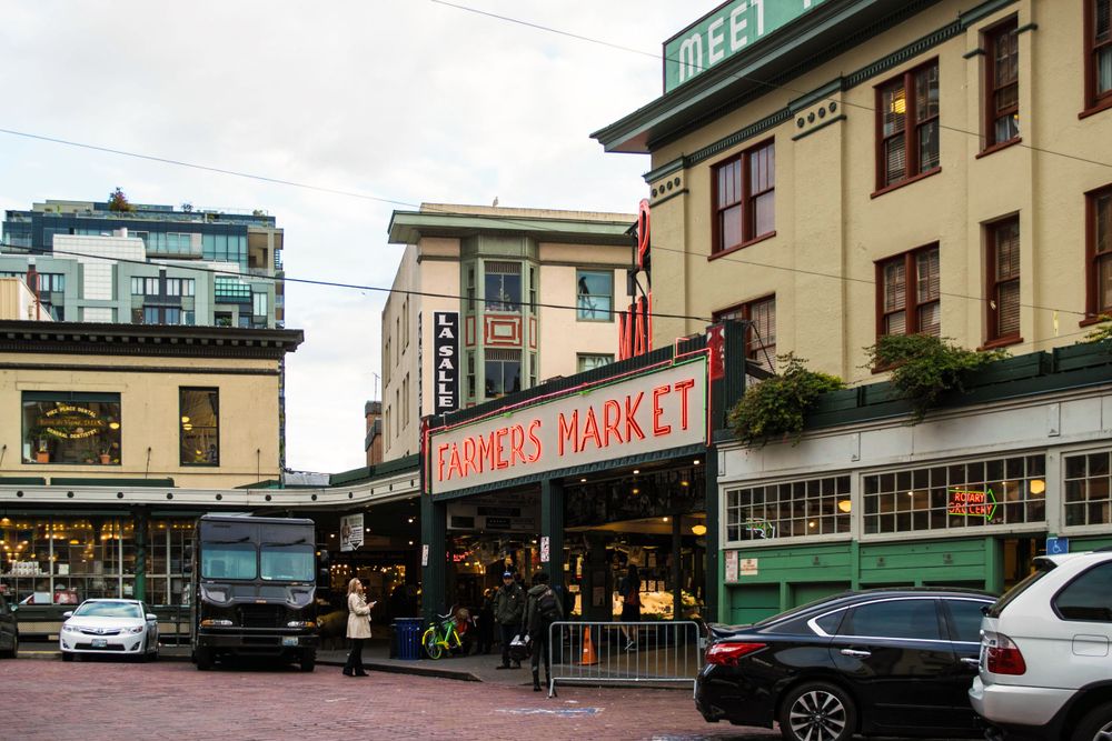 Exterior view of historic Pike Place Market building with traffic and parked cars.
