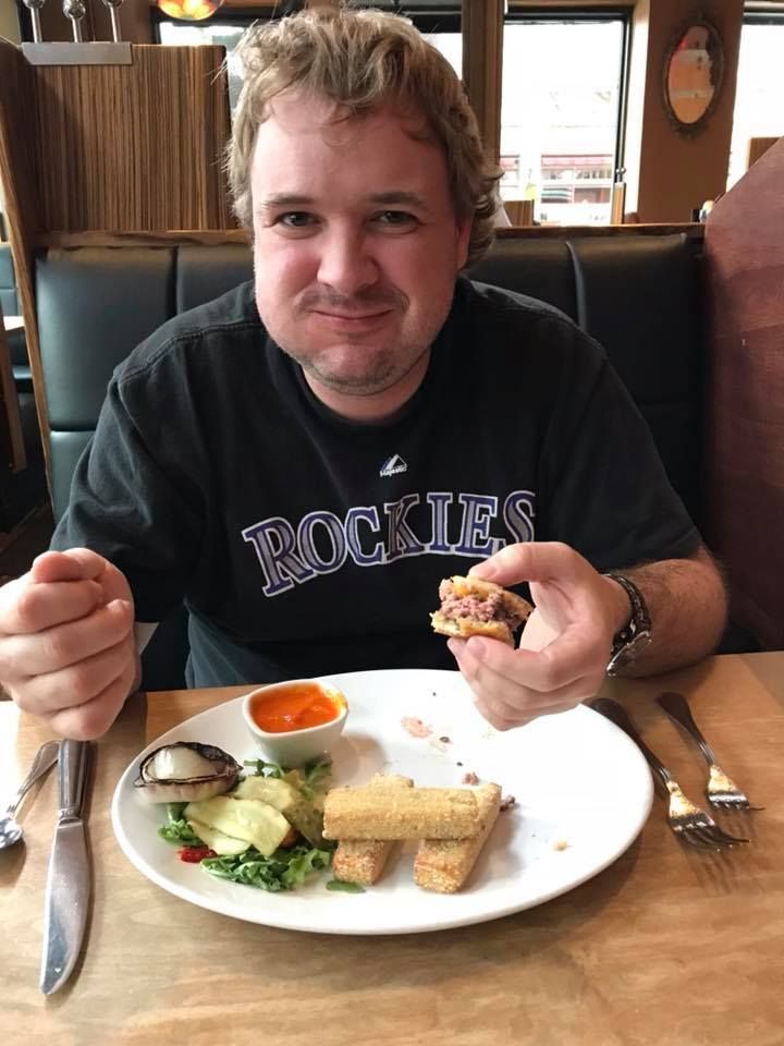 Restaurant patron in Rockies shirt enjoying a casual meal at a wooden table.