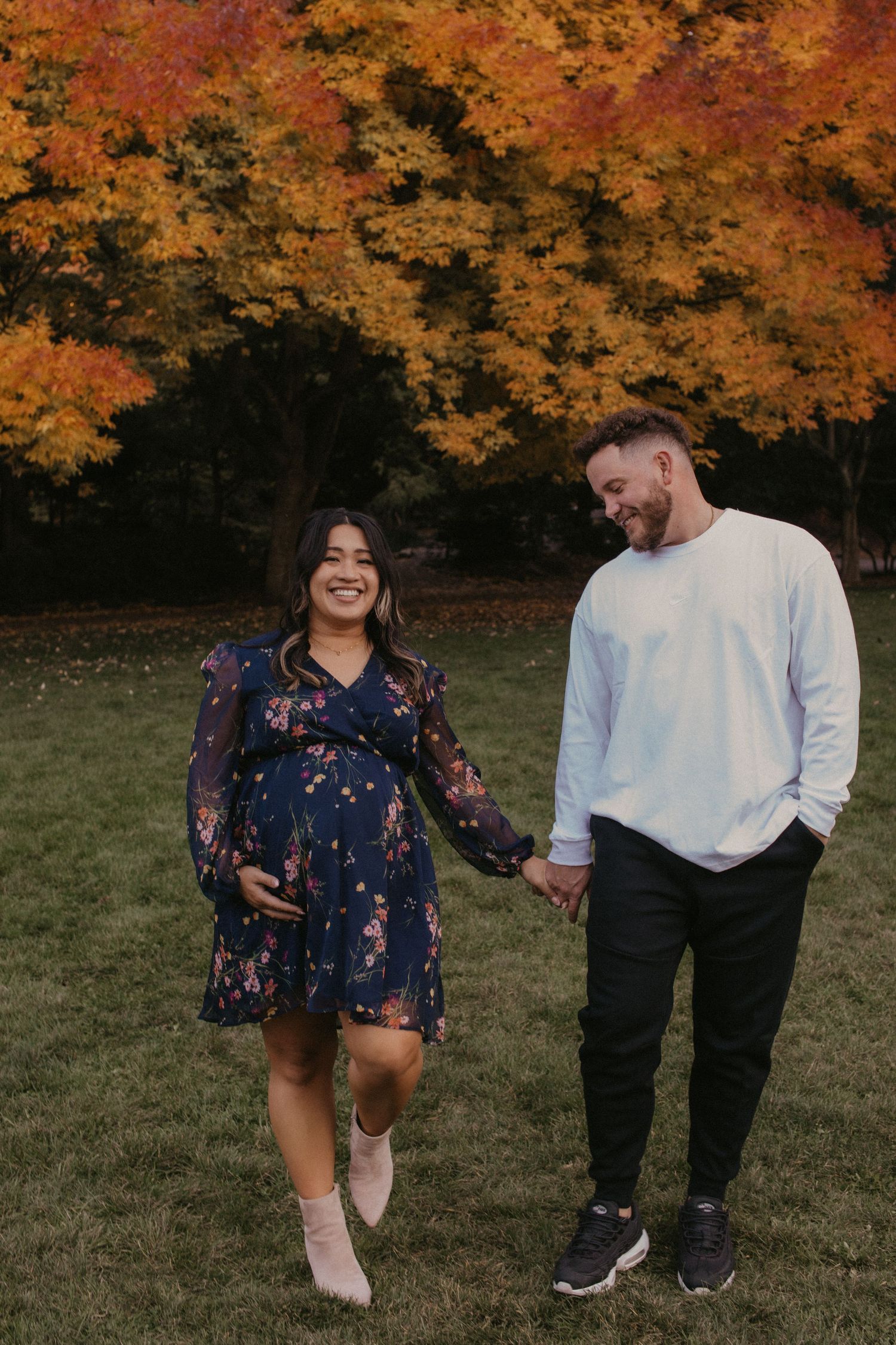 Couple walking and laughing together in autumn park with vibrant orange fall foliage in background.