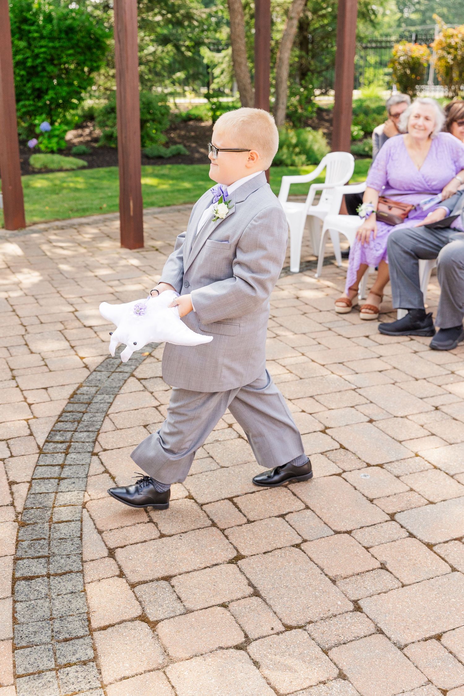 Young ring bearer in a gray suit walking along a curved brick pathway.