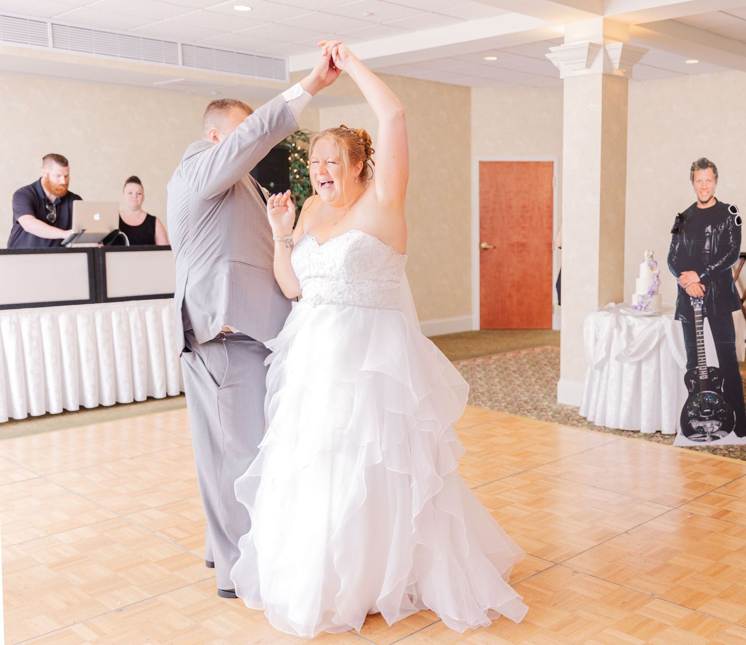 Wedding dance scene in reception hall with couple twirling on wood dance floor.