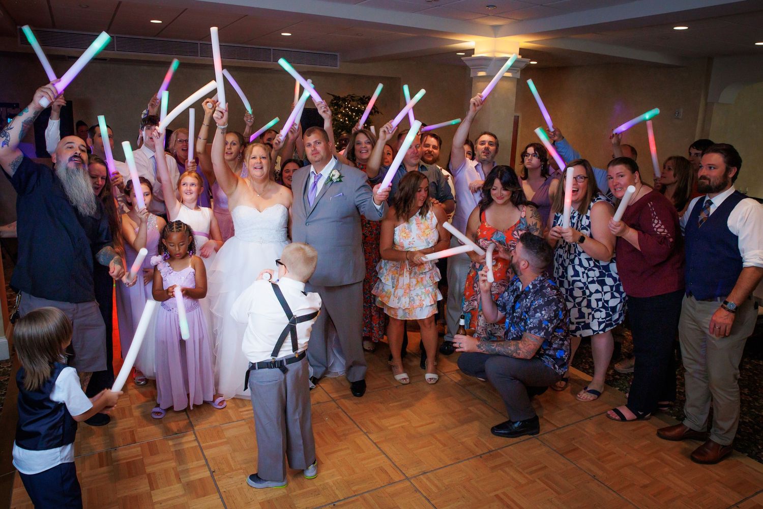 Wedding guests dancing with colorful LED light sticks on a reception dance floor.