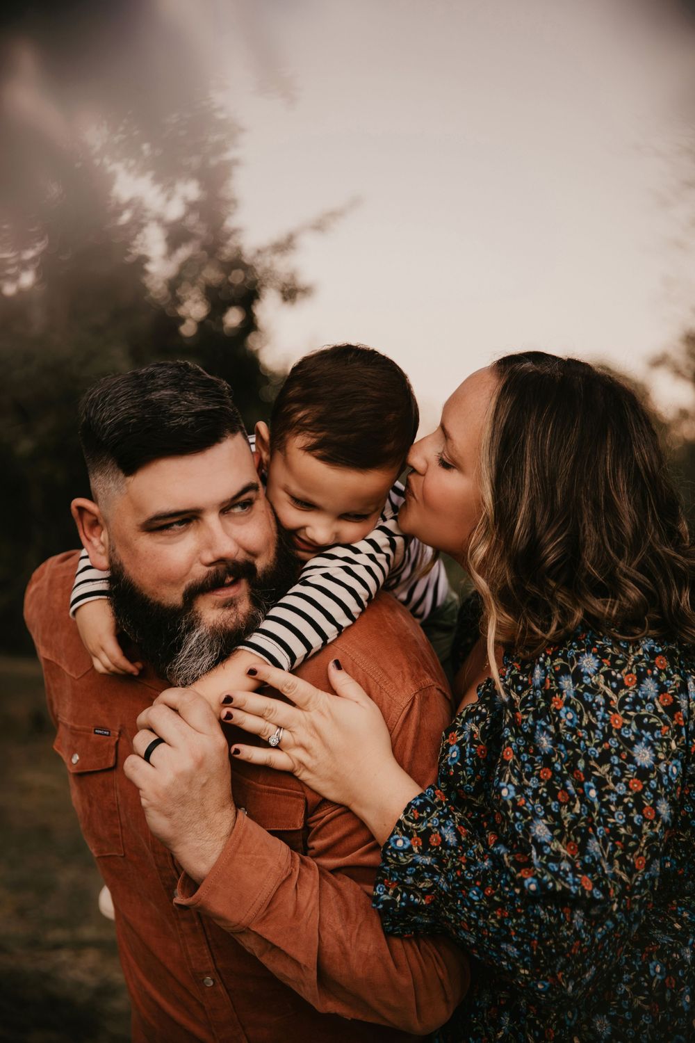 A tender family moment captured in warm sunset tones as parents share loving kisses with their child.