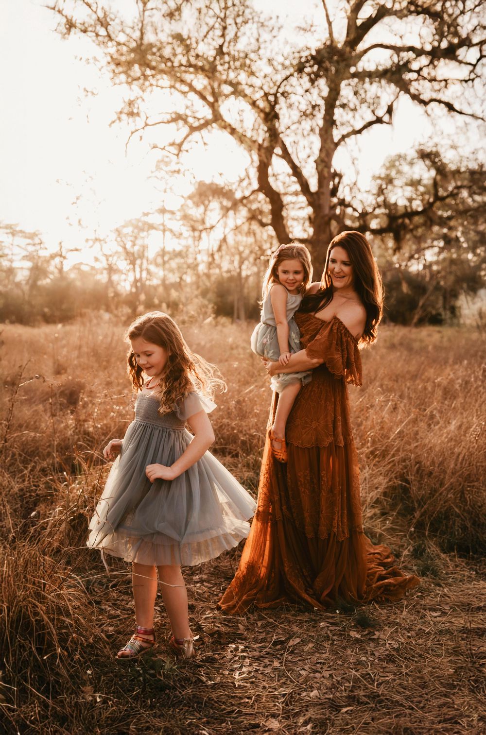 Warm sunset photoshoot in a field with people in gray tulle and rust-colored dresses creating dreamy portraits.