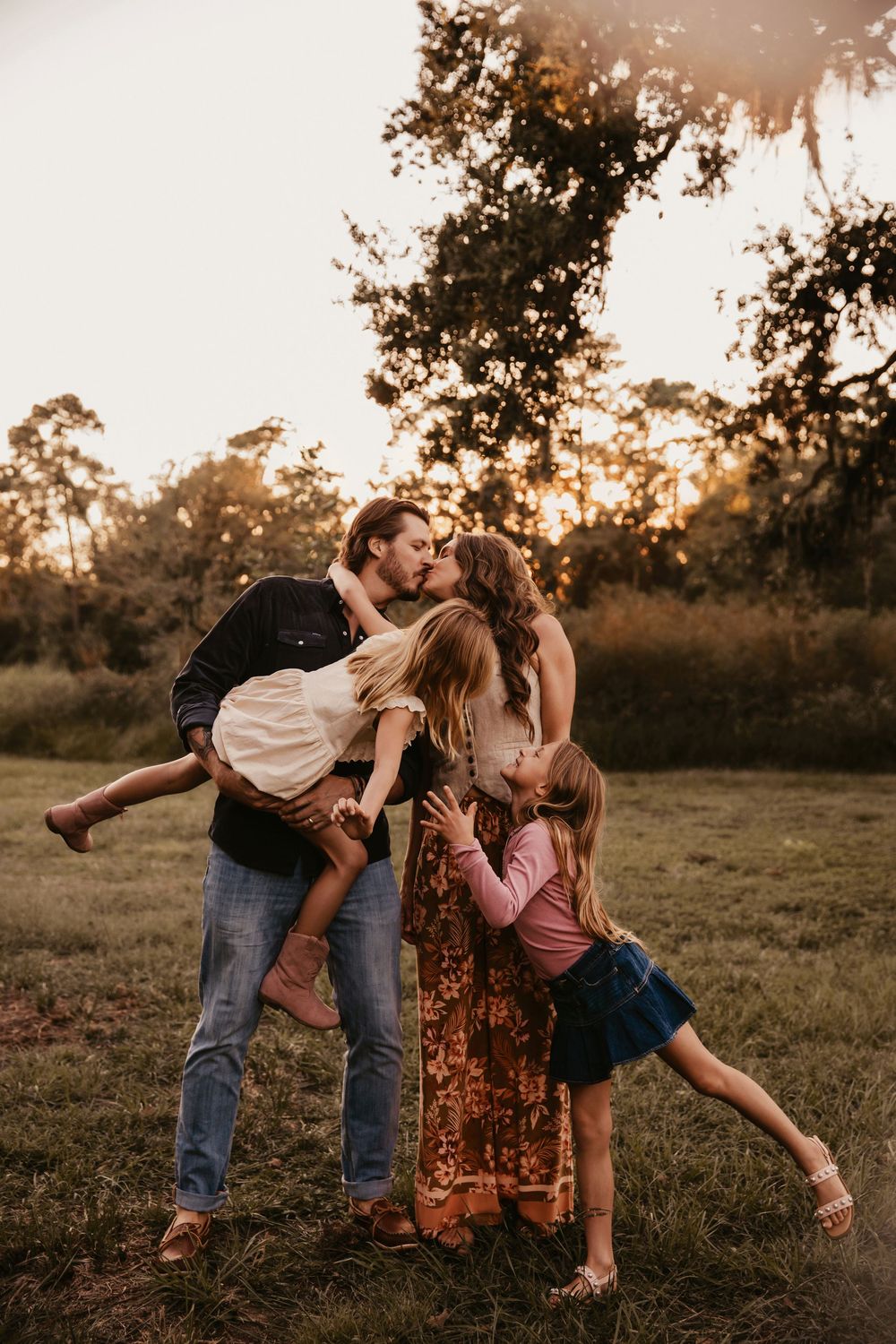 A family of four shares a playful embrace in a golden-lit field at sunset in a local Houston park