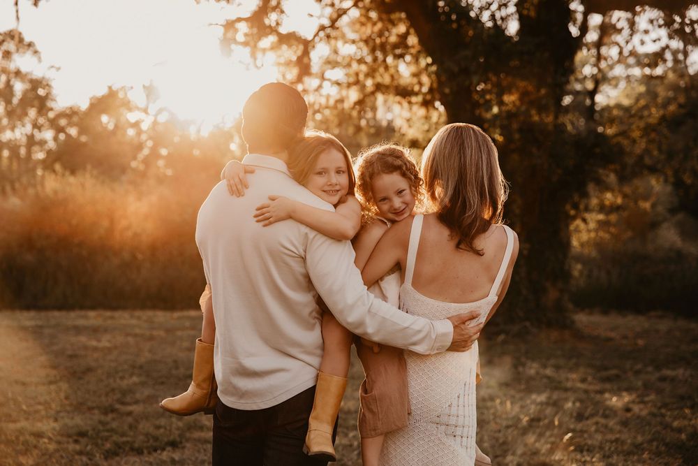 A couple embraces their children in a golden sunset field with warm autumn lighting creating a romantic silhouette.