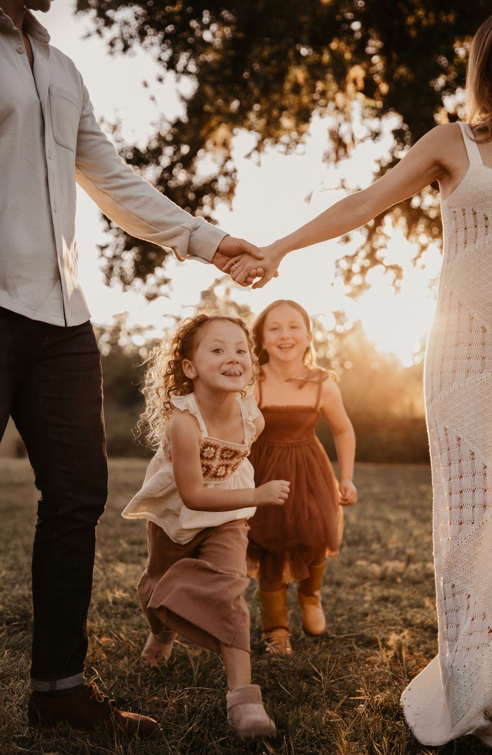 Children playing and running through a Houston field at sunset while their parents hold hands with adults in a candid photo series.