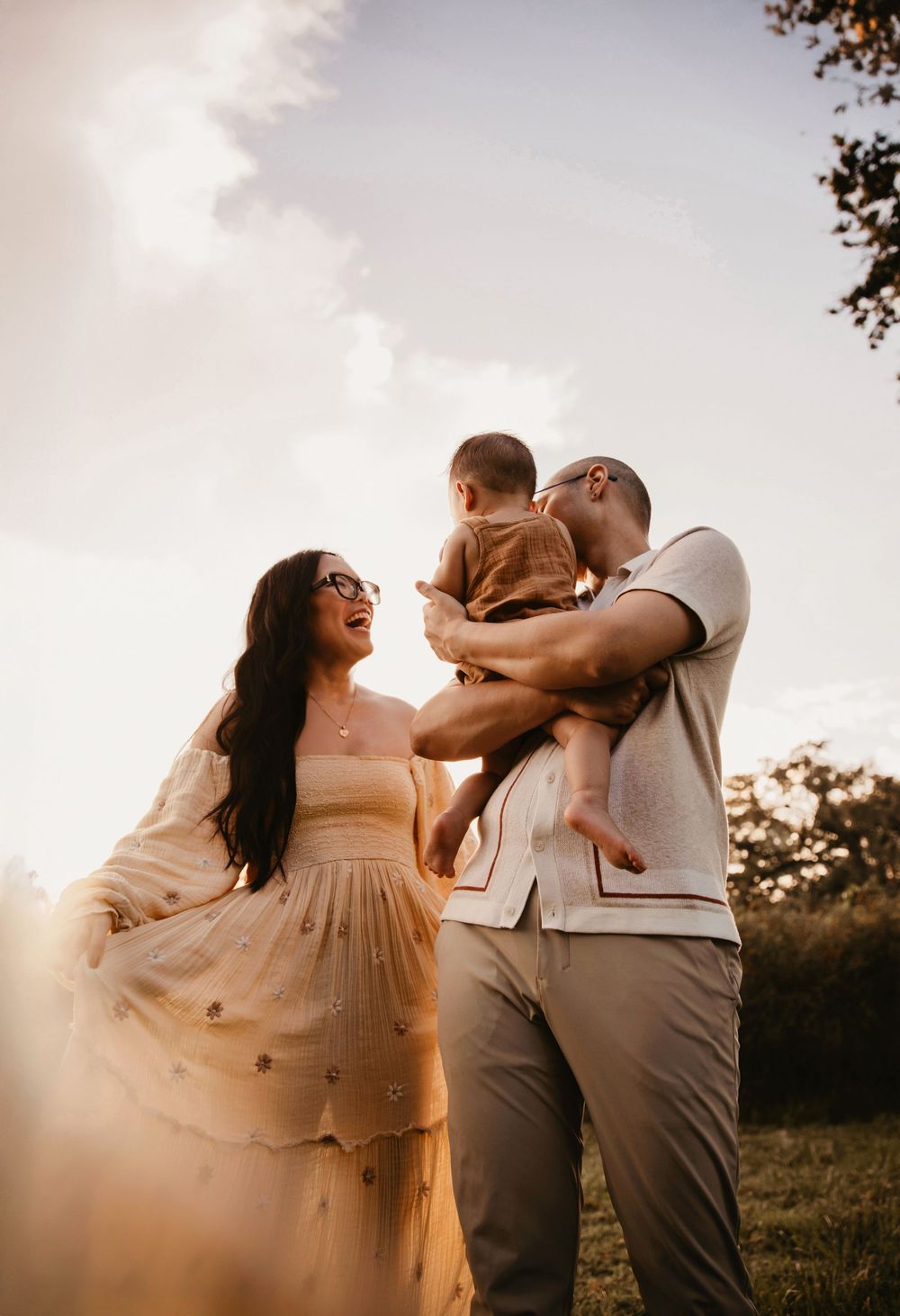 A family of three dances playfully in a golden sunlit field during sunset, creating a dreamy and joyful atmosphere.