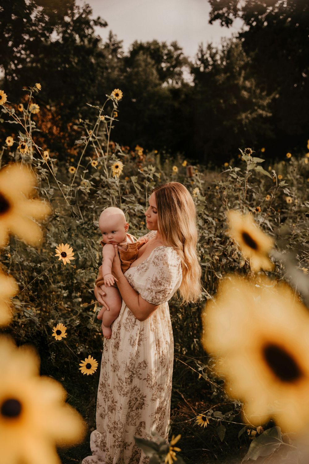 A dreamy mother and child country photoshoot amidst wild sunflowers during golden hour, with a floral style dress.