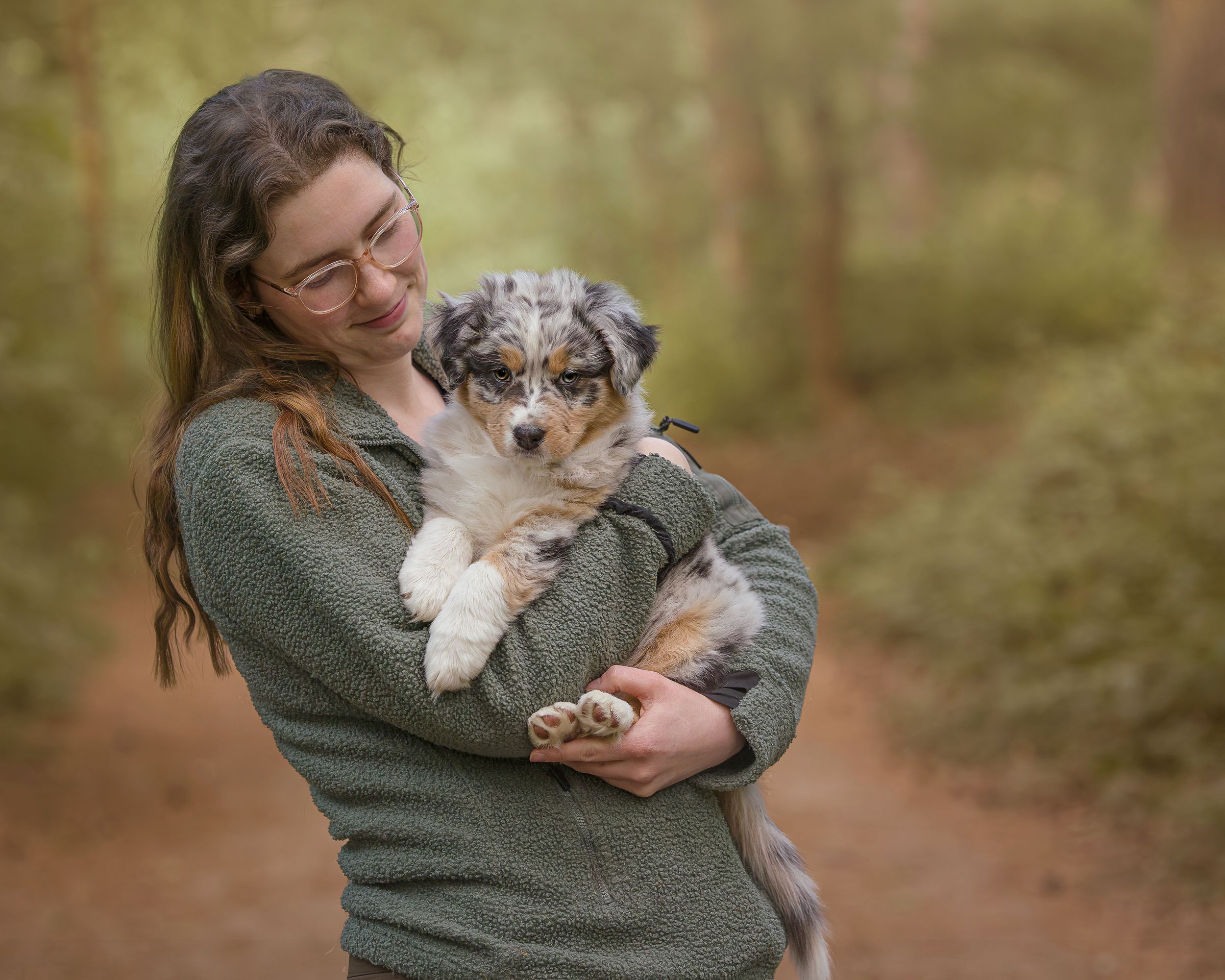 Australian shepherd dog being held and cuddled in someone's arms in a forest setting.