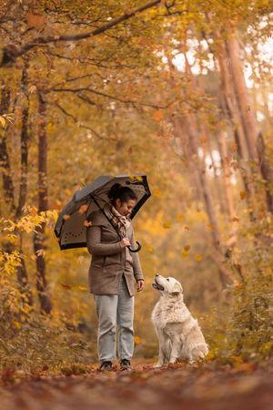 A dog and their companion share a moment on an autumn path under an umbrella.