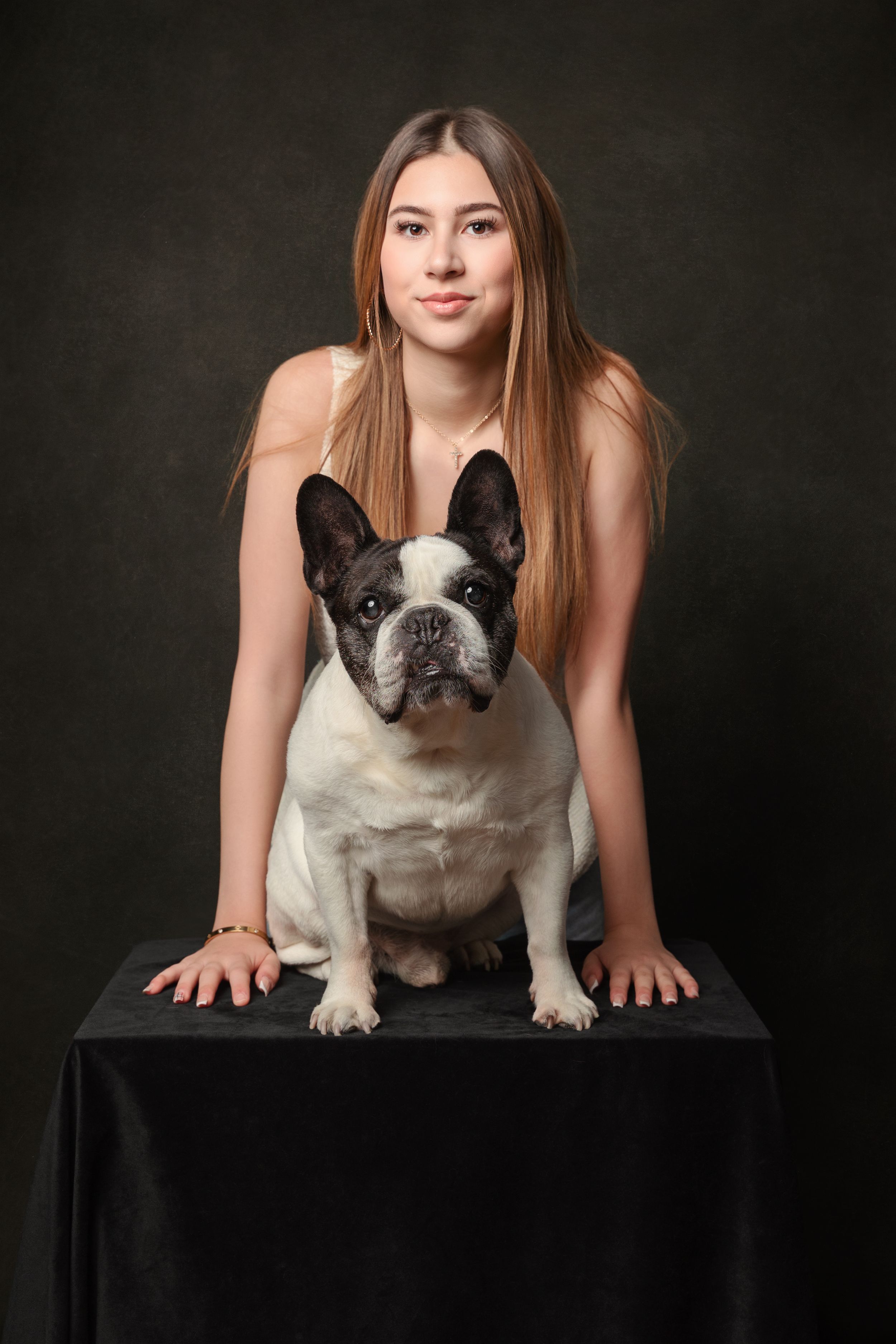 A French Bulldog sits on a black table against a dark background in a studio portrait.