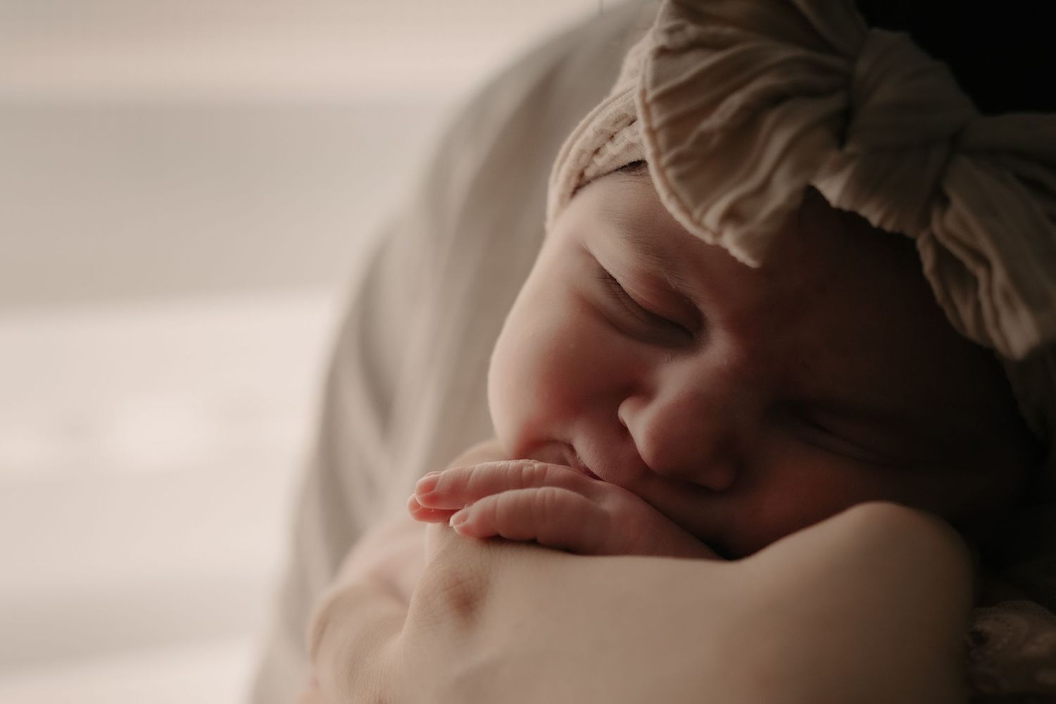 Sleeping baby with headband resting peacefully on white bedding.