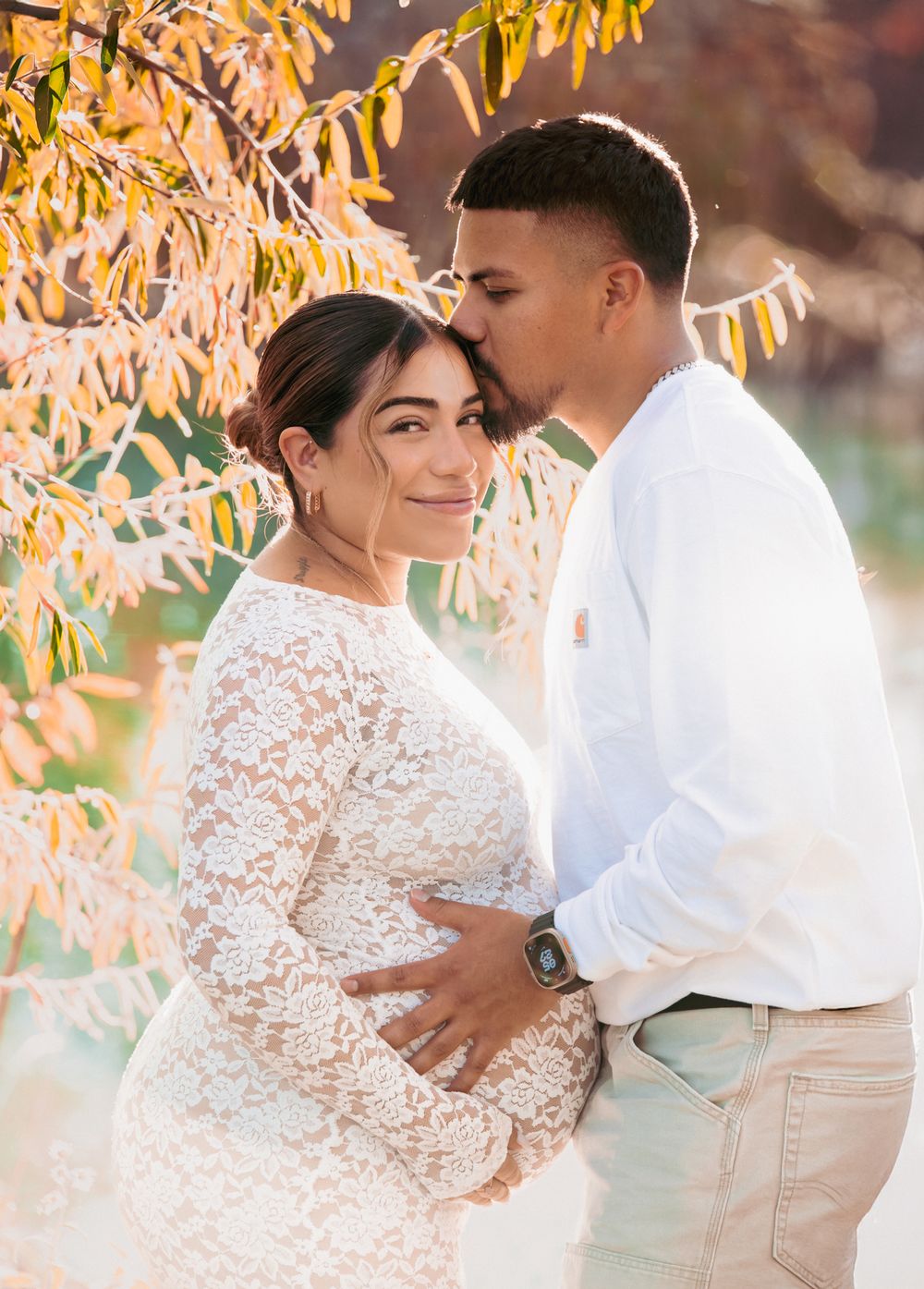 A romantic couple embraces under golden autumn leaves in a dreamy outdoor engagement photo session.