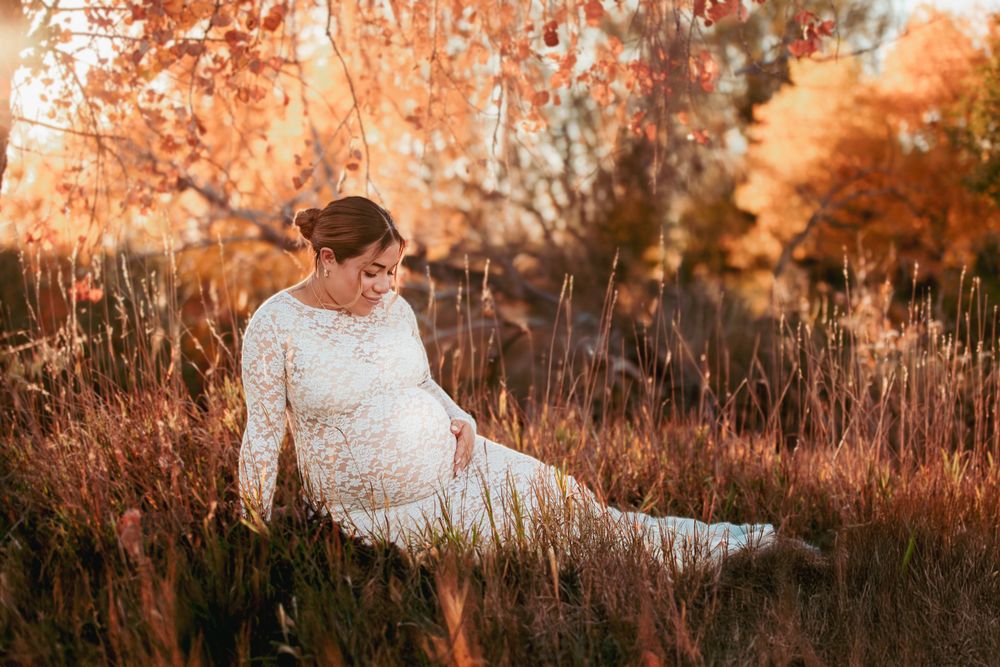 A bride in a white lace gown sits gracefully in a golden autumn field during sunset.