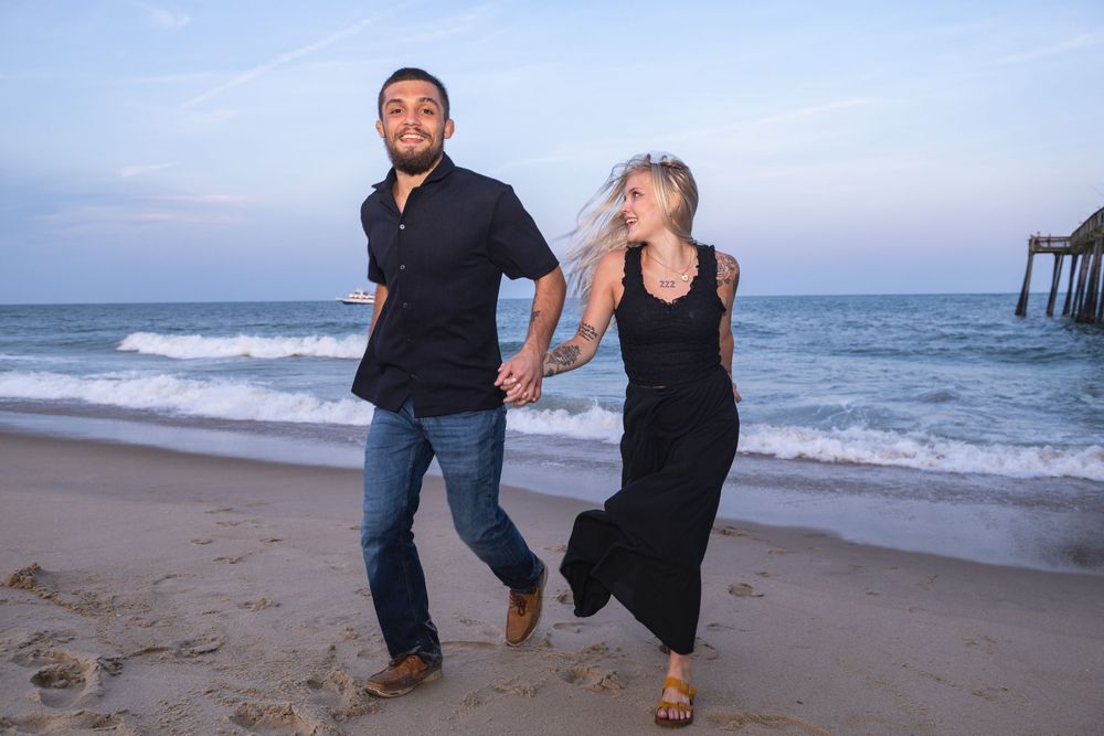 A couple shares playful moments together walking and posing along a sandy beach at sunset.