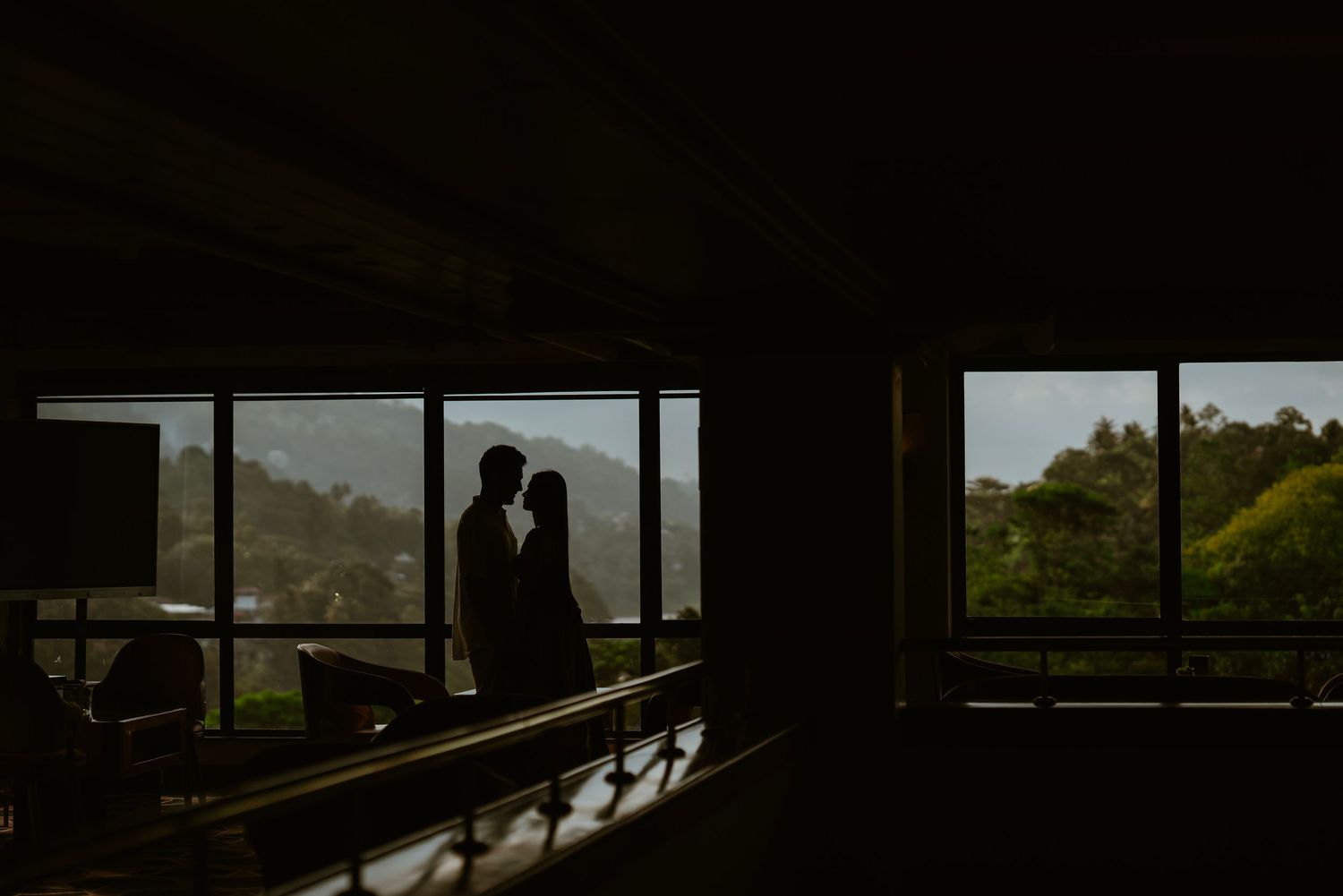 Silhouetted couple share intimate moments against dramatic window lighting in architectural setting.