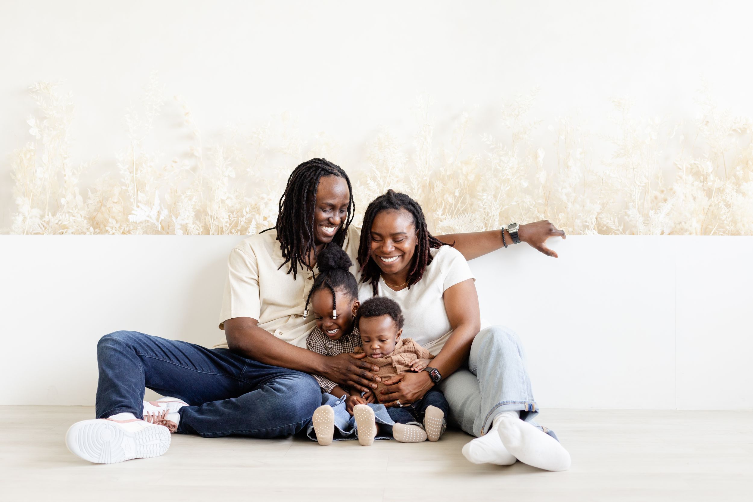 Family members laying on white floor wearing casual clothes while playing and laughing together.