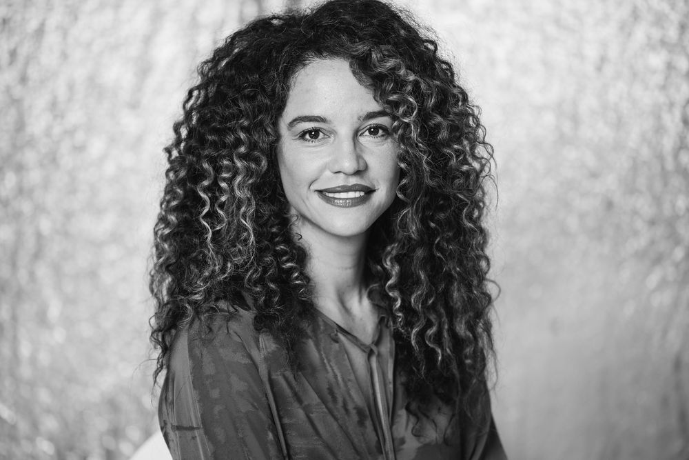 Black and white portrait of a young woman with long curly hair, smiling warmly at the camera.